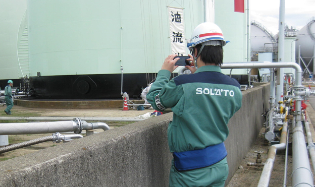 画像：発災現場を、RICOH UCSが入ったスマートフォンで撮影。防災訓練では、現場から四国事業所の防災本部と、東京本社へリアルタイムに災害の映像を配信。