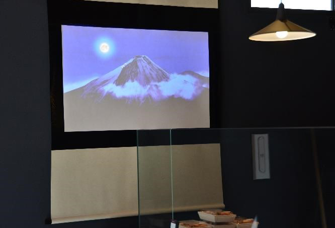 画像：築地直売所でもプロジェクターを使った、店舗演出を実施。掛け軸風のスクリーンに映像を投影。