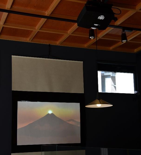 画像：天井からプロジェクターを吊るして、掛け軸風のスクリーンに映像を投影。（築地直売所）
