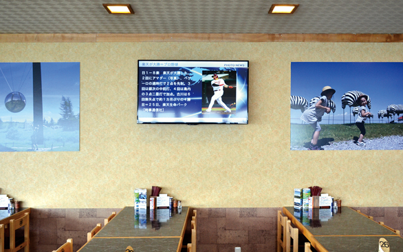 画像：人が多く集まる道の駅内のレストランにモニターを設置。モニターの両サイドに写真も掲示し、壁面を情報配信の場として有効活用しています。
