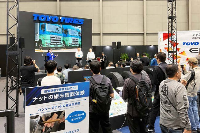 2026ジャパントラックショーのTOYO TIRESブースではリトレッドタイヤが展示され、イベントでは髙瀨商会の小池執行役員も登壇（登壇男性左）
