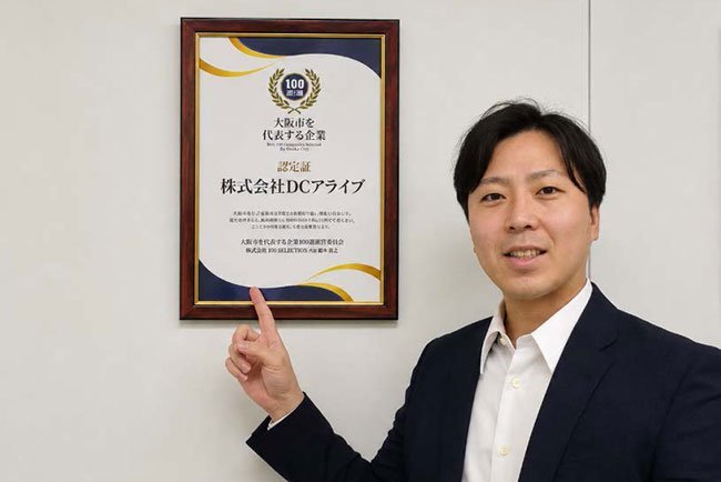 「大阪市を代表する企業」の認定証を前に撮影に応じる水主誠社長