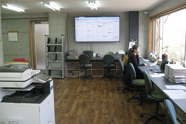 ミネックのオフィスの様子(手前に複合機、正面に社員のスケジュールを表示した電子黒板)