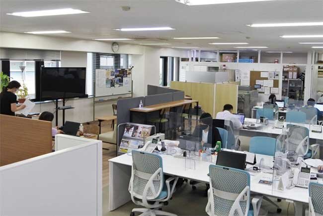 フリーアドレスの職場。左手にハドルスペースが見える。左の奥に見える電子黒板で研修や打ち合わせを行う