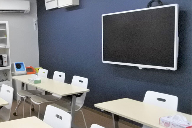 食事エリアの壁には電子黒板。テーブルをコの字形に並べ変えるとミーティングルームに早変わりする