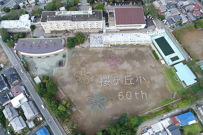ドローンで撮影した、同社の近隣小学校【開校60周年記念】（子どもたちのデザインをもとにGoogleEarth上でデータを作成、測量の特別授業にて制作）