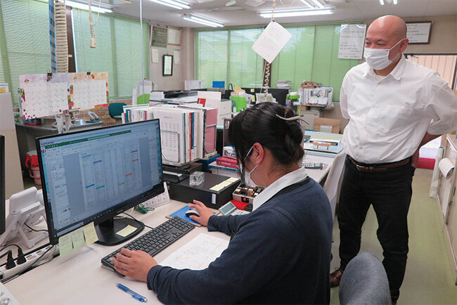 1台に集約されたパソコンで業務中の従業員と水野社長