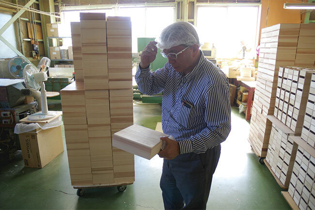 おせち料理を入れる木箱を手に取る八木代表取締役