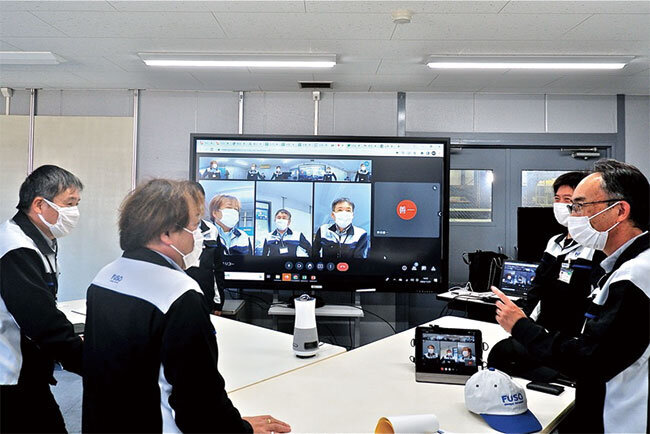 360°カメラを囲み、他工場の参加者も映る大型モニターを使ったリモート会議