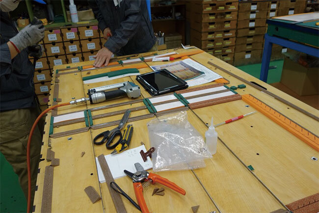 段ボールと抜型がくっつかないように刃物の周りにゴムをつける作業。タブレットで図面を確認しながら作業をしている