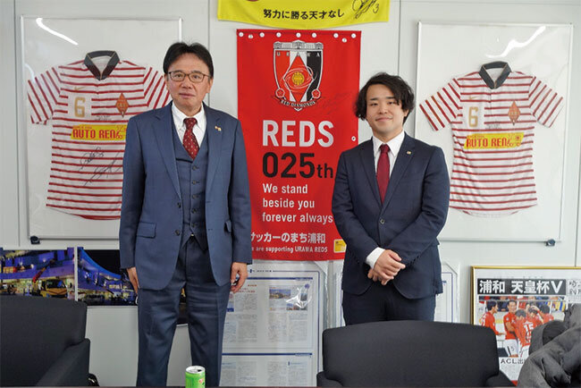 上野親子が並ぶ応接室の壁には浦和レッドダイヤモンズのグッズ類。地域貢献の一環として2012年からファミリーパートナーを務めている