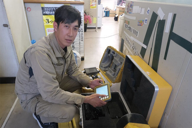 三次元設計図面をもとに建機を自動制御する装置を手にする鶴留専務