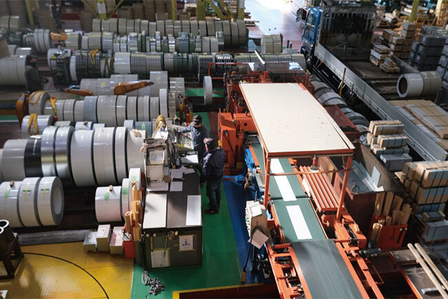 コイル状の鋼板から切り出され、ベルトコンベヤー上を流れていく加工済の商品。板取システムによってムダのないよう切り出されている