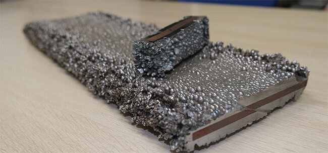 展示品として保管されている、分厚くクロムめっきされた鉄材。茶色の部分が鉄材で、その周りをクロムが覆い、表面にはコブができている。実際にはめっき厚5～数百μmが施され、研磨作業で鏡面にする。