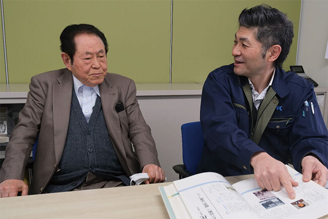 古市仁会長（左）と、会長の入社当時の写真が載っている50年史を示す古市光社長。仁会長は「若いころに高速撹拌機の営業をしていたころが一番楽しかった」と話した