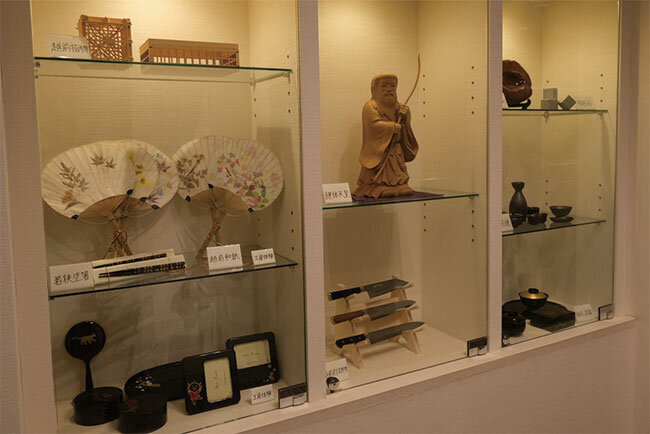 福井県内7つの伝統工芸が並ぶエレベーター前の飾り棚。作家の作品だけでなく、社員の作品も並べられている