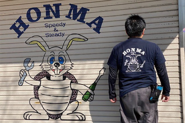 Tシャツの背中と会社前のシャッターにはロゴマークが印されている