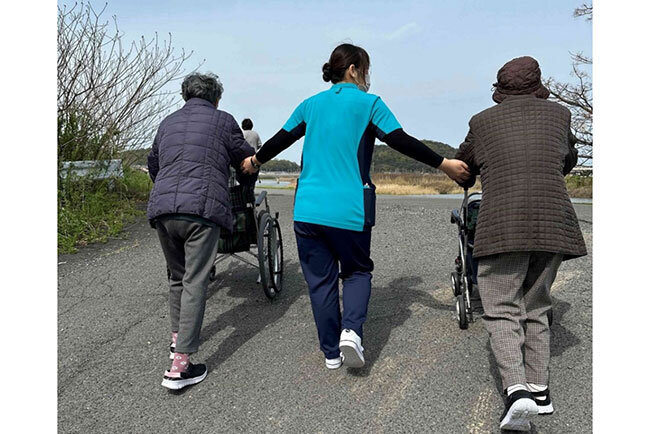 車いすを押して近くの川の土手を散歩する入所者と介護職員
