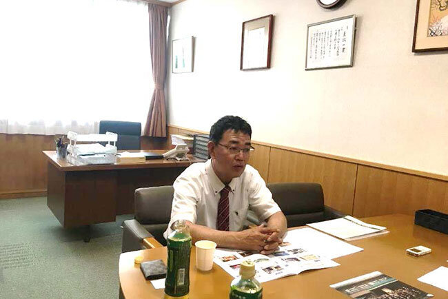 入社当時の集合写真を前に話す小須田施設長
