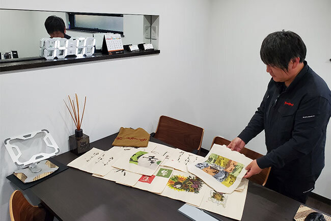 切り絵作品などをプリントした布製品を紹介する山本社長。衣類に直接プリントできる