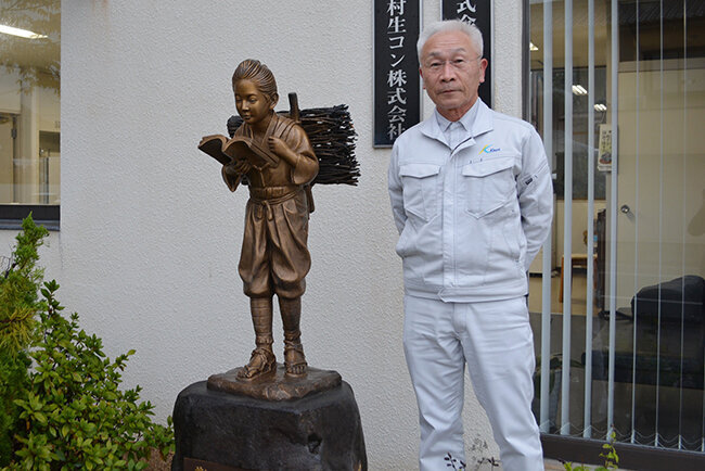 本社玄関脇の二宮金次郎像を見ながら経営理念「勤・倹・譲」について話す木村社長