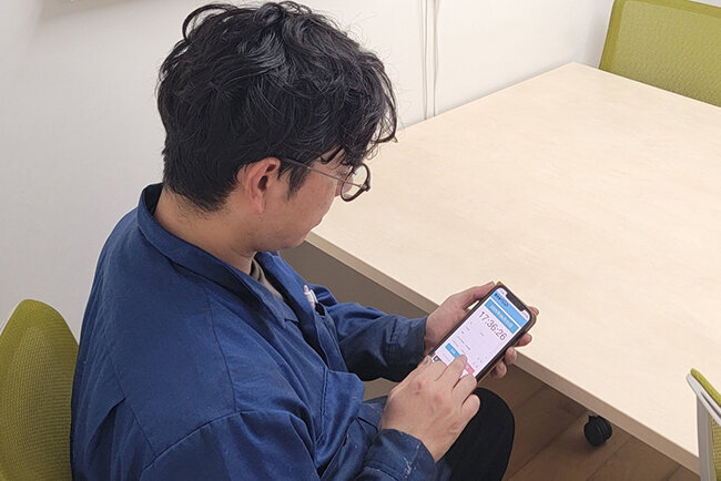 退勤時間をスマートフォンで打刻する従業員。そのままタイムレコーダーに記録される