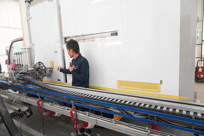 大型オートボディプリンターを使ってトラック車体へのプリント作業に取り組む様子