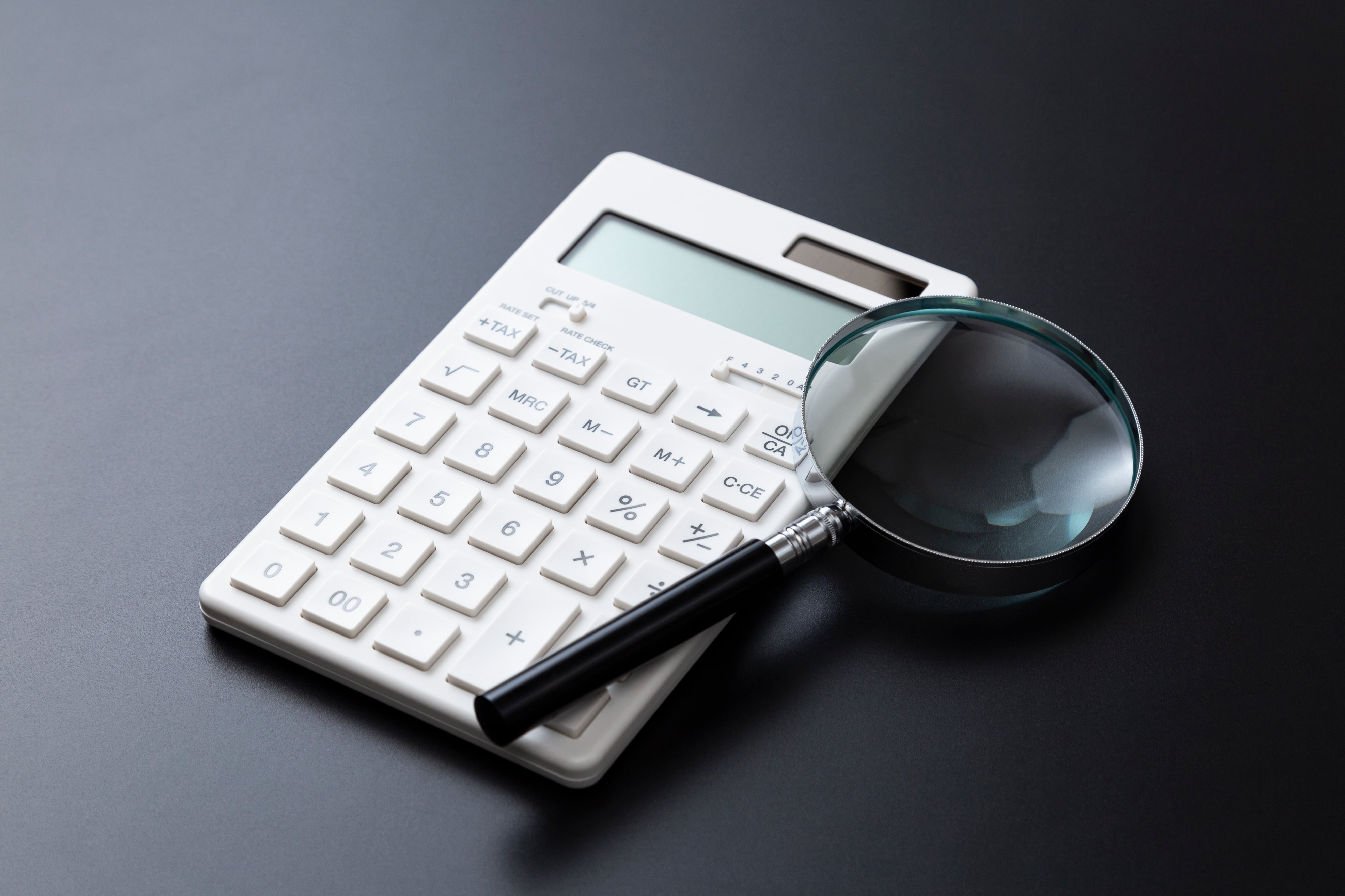 電卓と虫眼鏡が並べて置かれている写真。 決算書の内容を詳しく確認・分析することをイメージさせる構図。