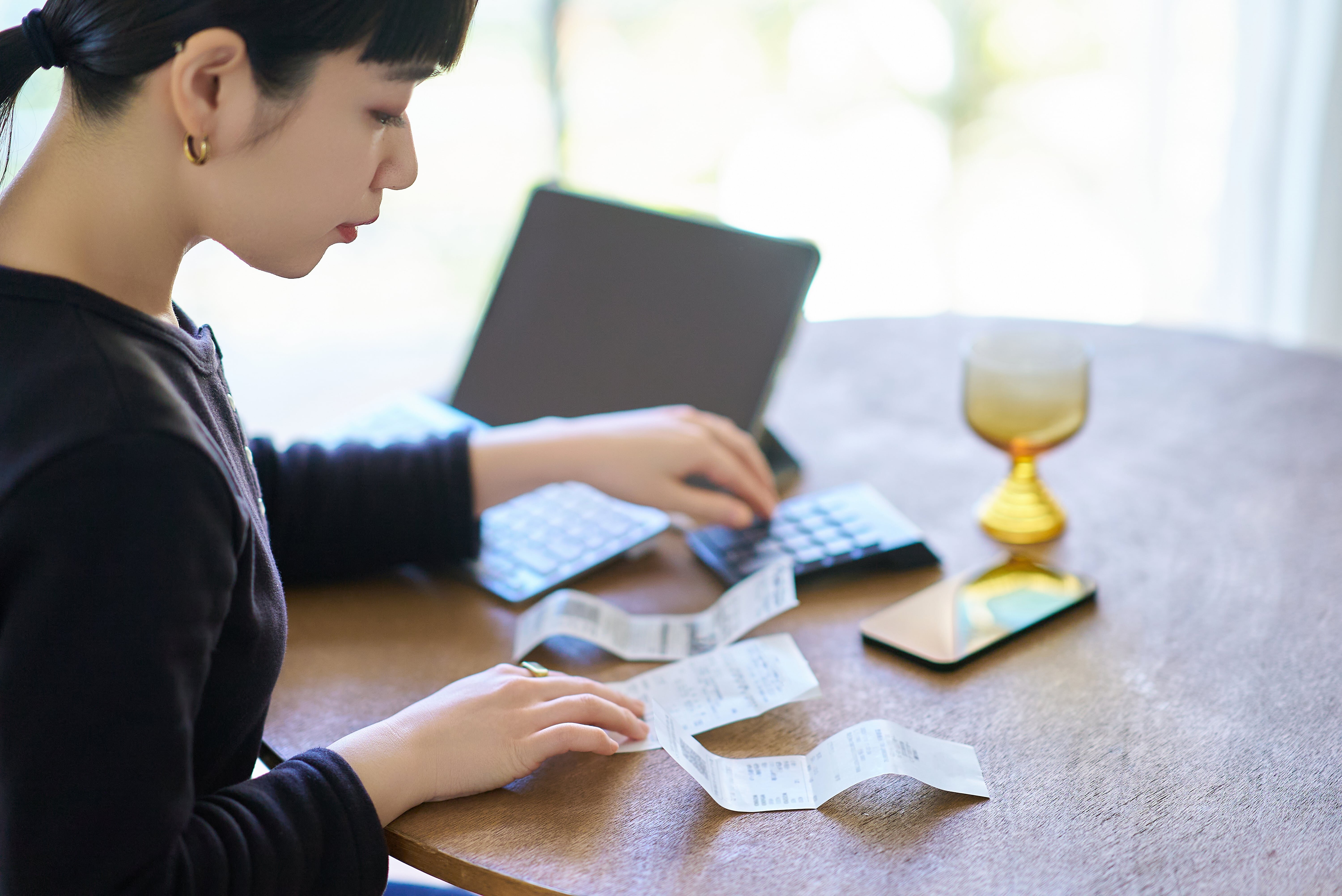 領収書やレシートを確認しながら家計管理を行う女性の様子。領収書の基本的な役割や項目を解説する内容に関連したイメージです。