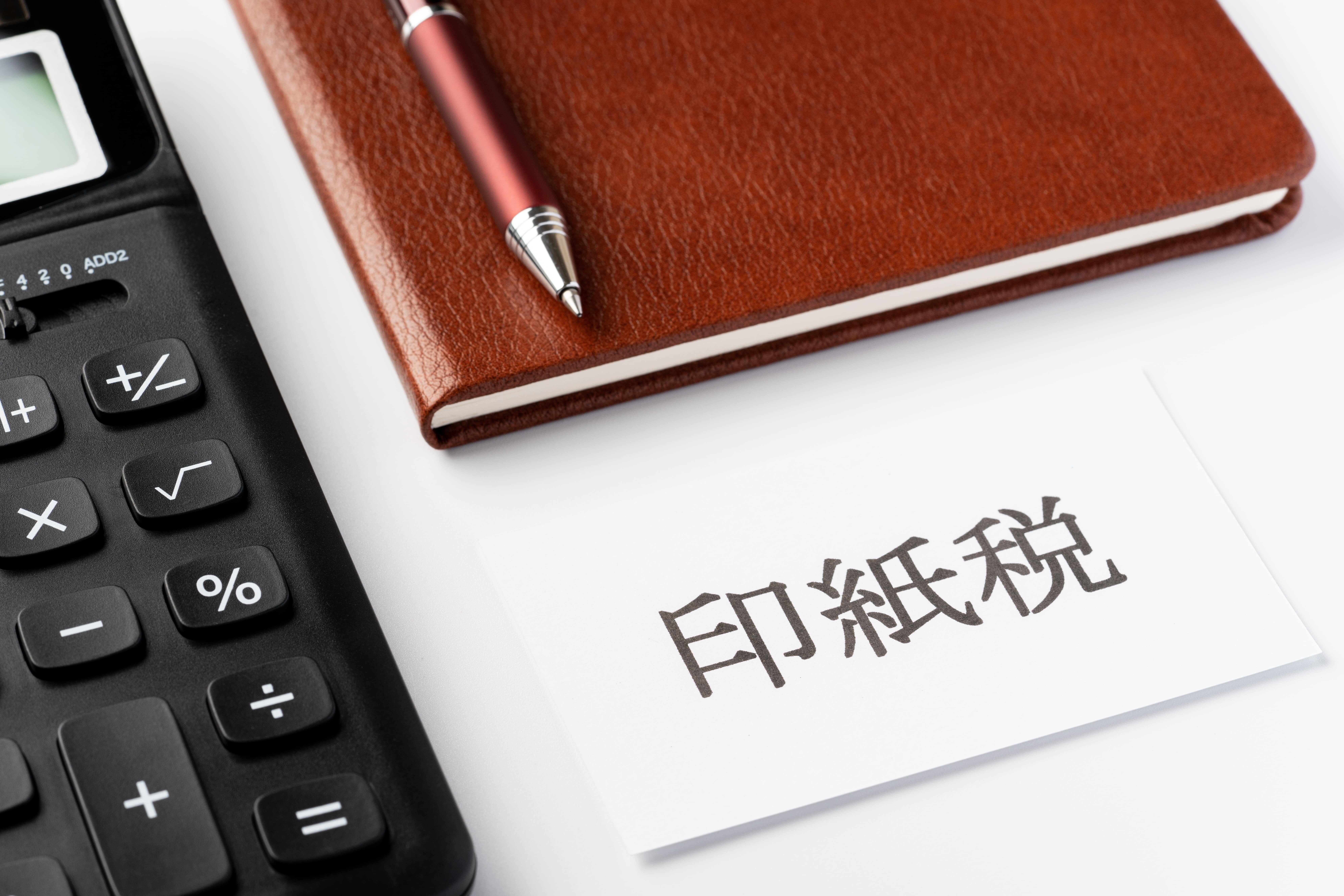 電卓と手帳、そして「印紙税」と書かれたカードを並べたイメージ。領収書に貼付する収入印紙や印紙税に関する説明を示しています。