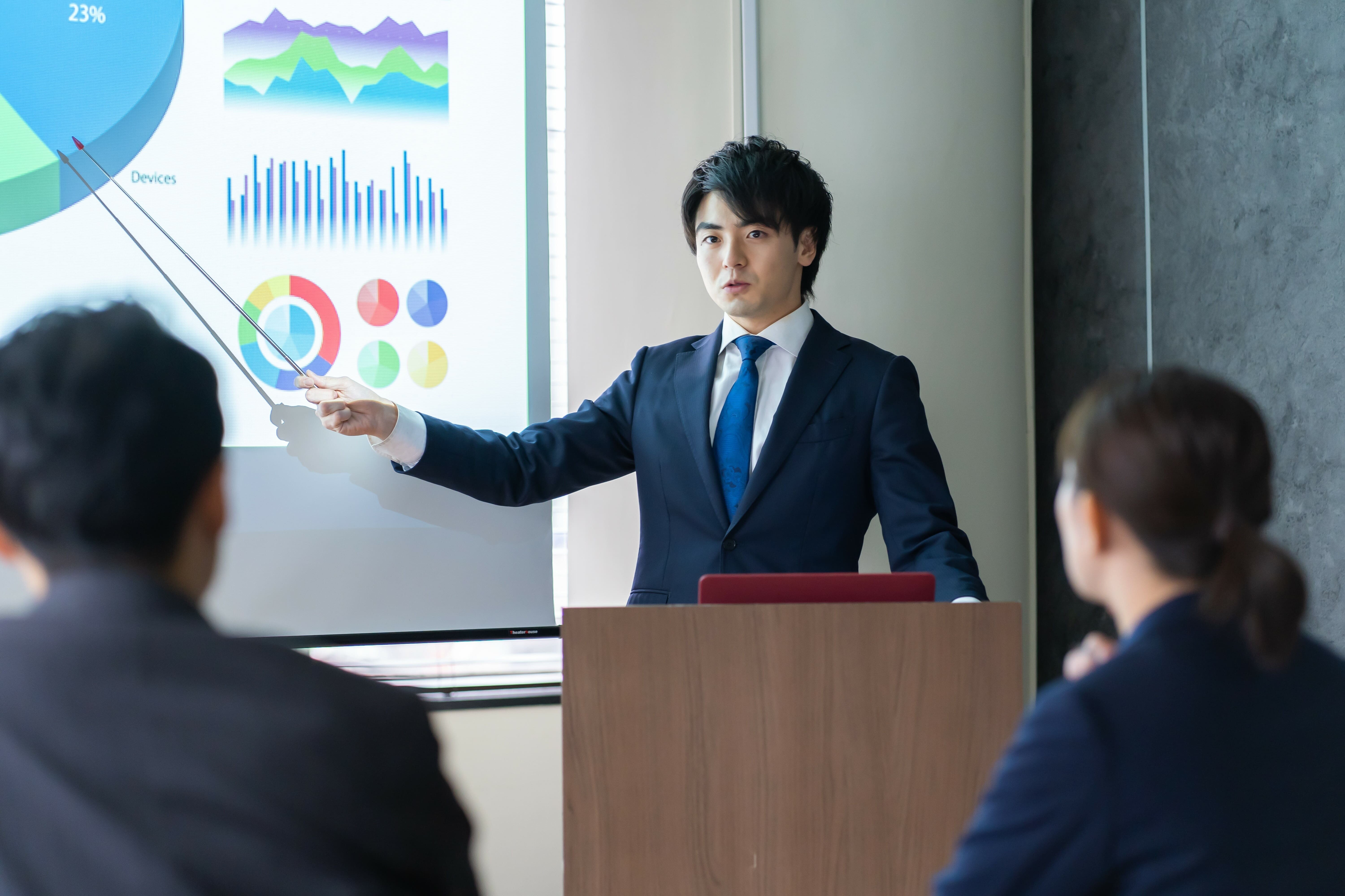 スーツ姿の男性がプレゼンでグラフを指し示している写真。 ハロー効果のように、第一印象や見た目が評価に影響する心理現象を象徴する。