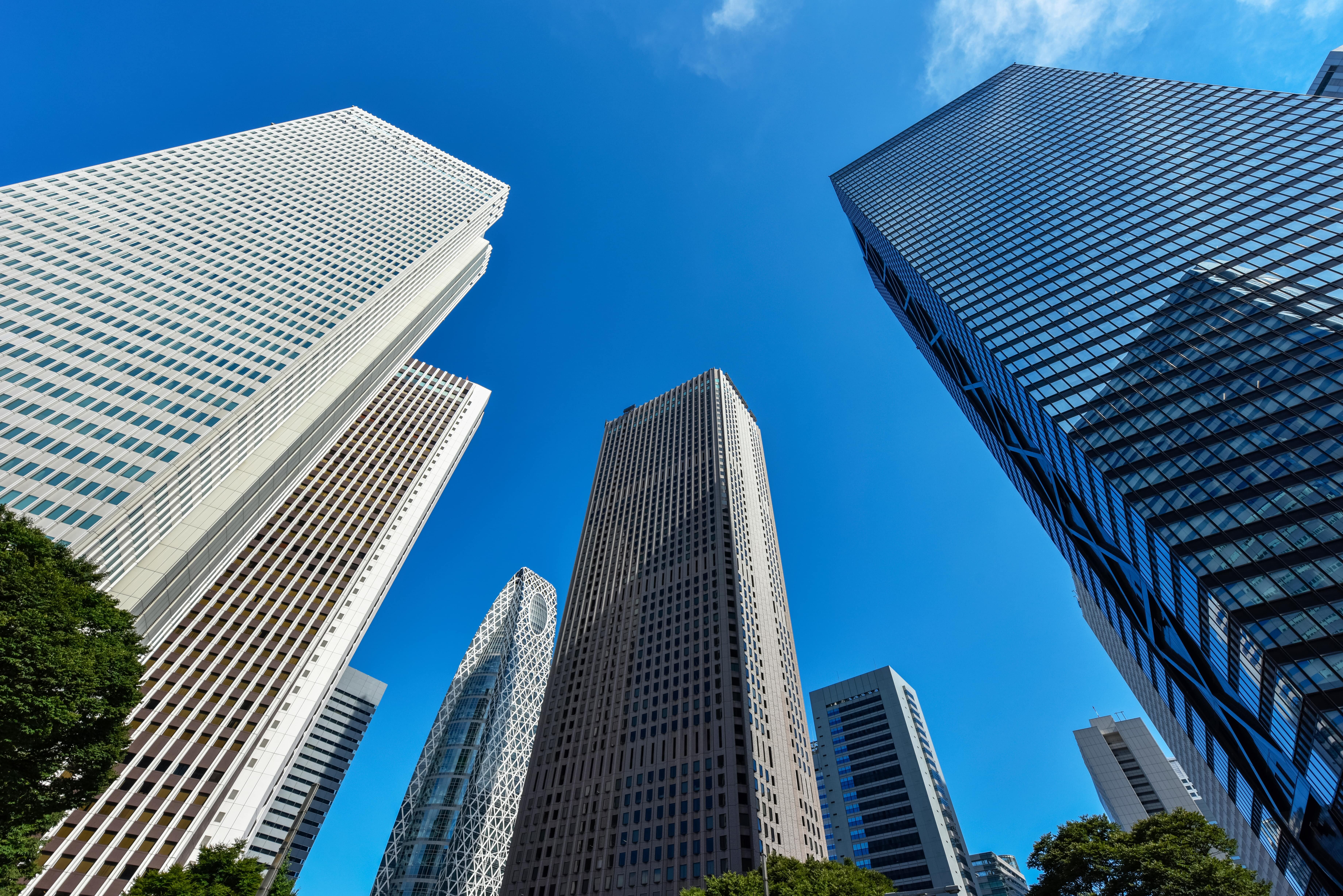 高層ビル群を下から見上げた写真。青空とガラス張りのオフィスビルが映り、企業や労働環境をイメージさせる。