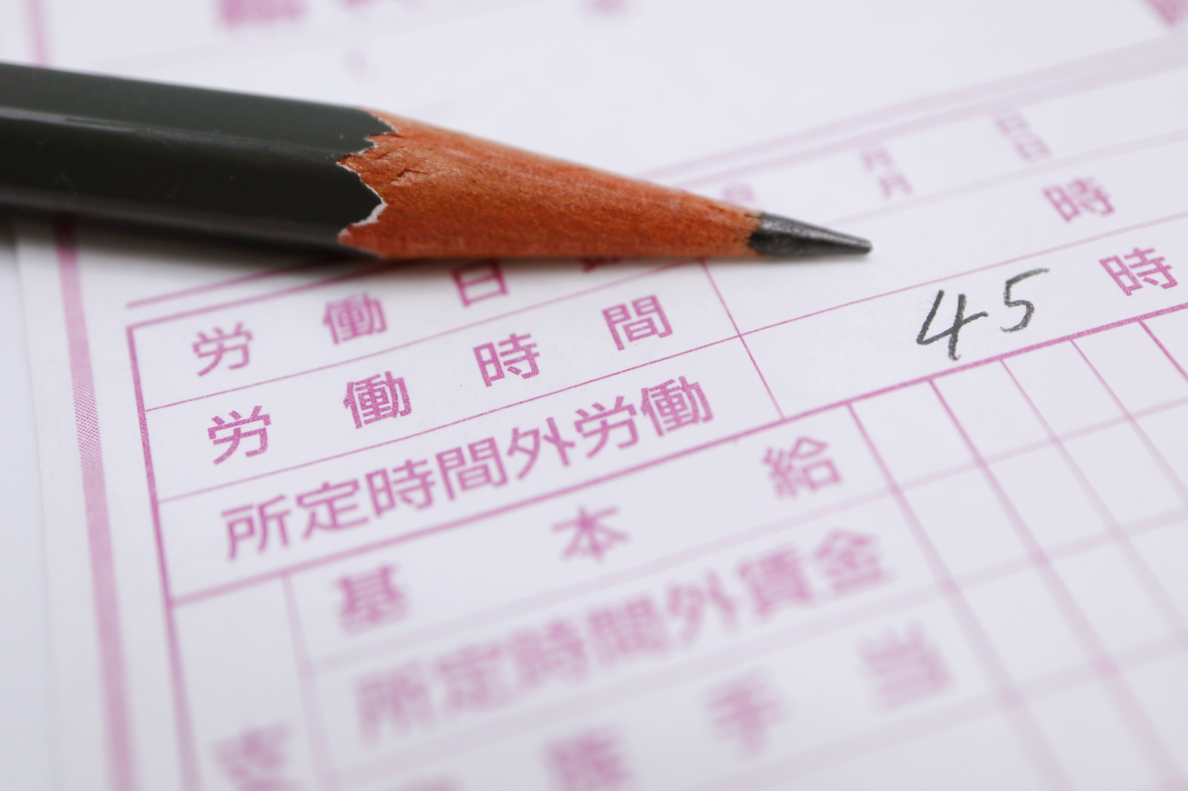 労働時間や残業時間が記載された勤怠管理表に鉛筆で『45時間』と書き込まれている写真。残業時間の上限や特別条項をイメージさせる。