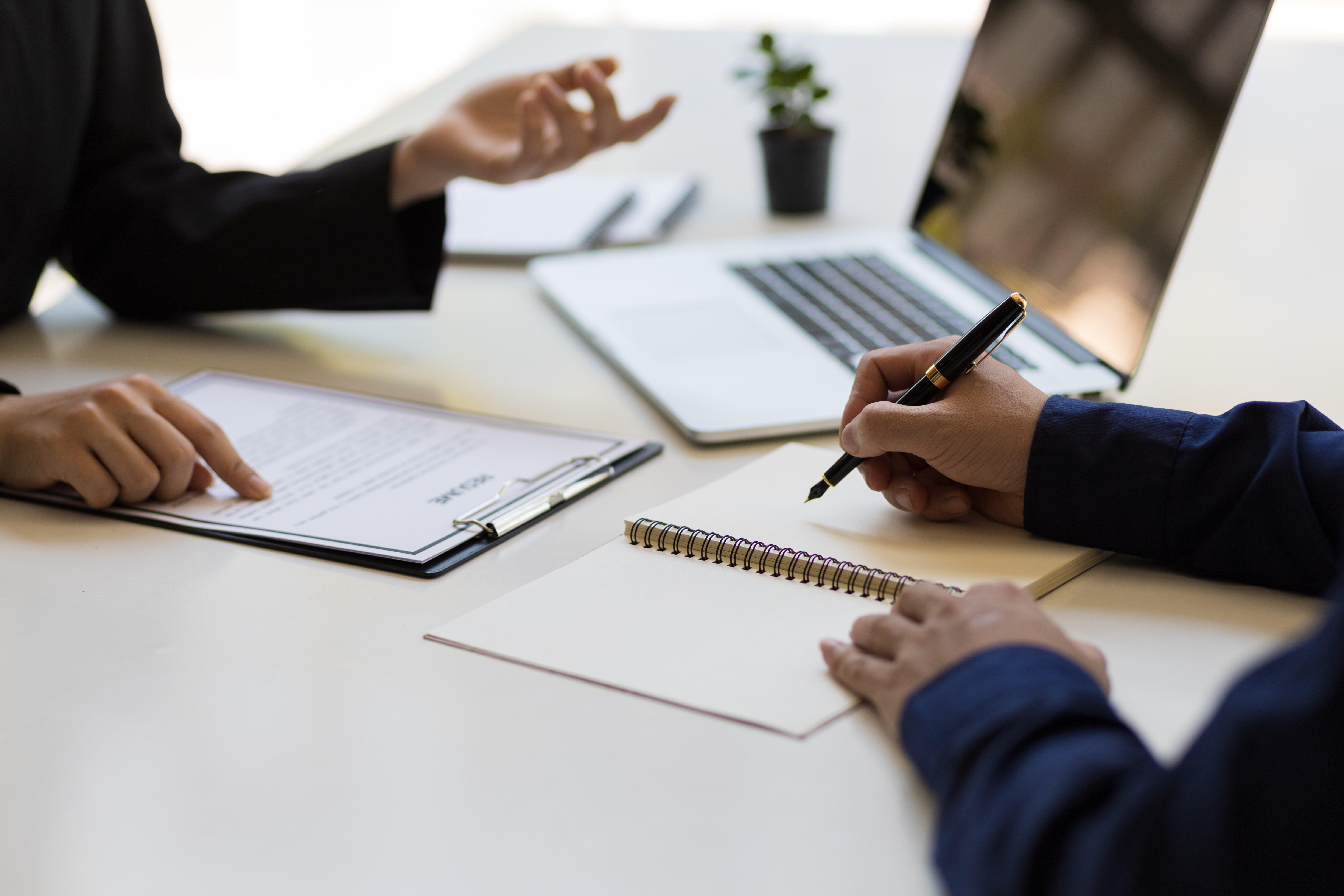 机を挟んで打ち合わせをしている2人の手元の写真。書類とメモを取りながらBCP作成について話し合っているイメージ。