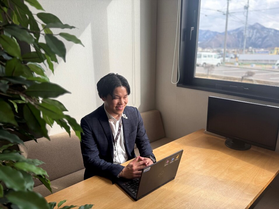 笑顔でインタビューを受けるりょうすけさん(ちらりと長野の山)