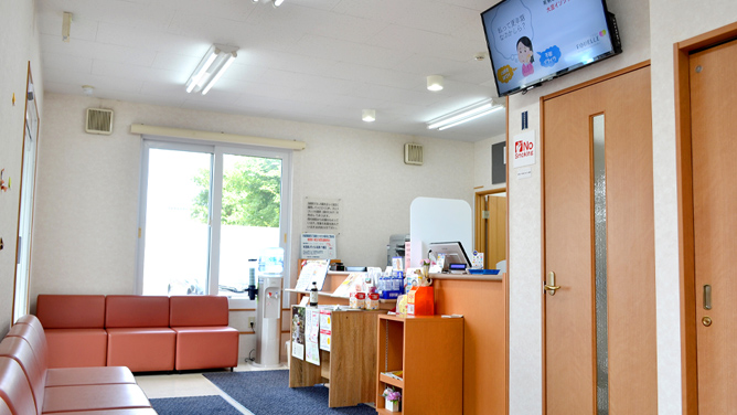 デジタルサイネージが扉上に設置された病院の待合室の画像